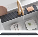 Dark gray diatomite stone faucet mat with a rectangular shape, placed around a kitchen sink faucet with items on it.
