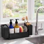 Black sponge holder for kitchen sink with a white drying stone and two removable cups, holding sponges and brushes.