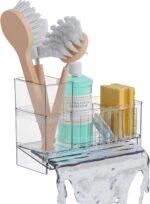A clear plastic SuoXing sink caddy with multiple compartments holding sponges, a dish brush, and soap bottles.