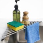 Gray Tomorotec triangle roll-up dish drying rack extended over a sink corner with dishes and sponges on it.
