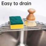 Gray Tomorotec triangle roll-up dish drying rack extended over a sink corner with dishes and sponges on it.