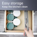 Gray Tomorotec triangle roll-up dish drying rack extended over a sink corner with dishes and sponges on it.